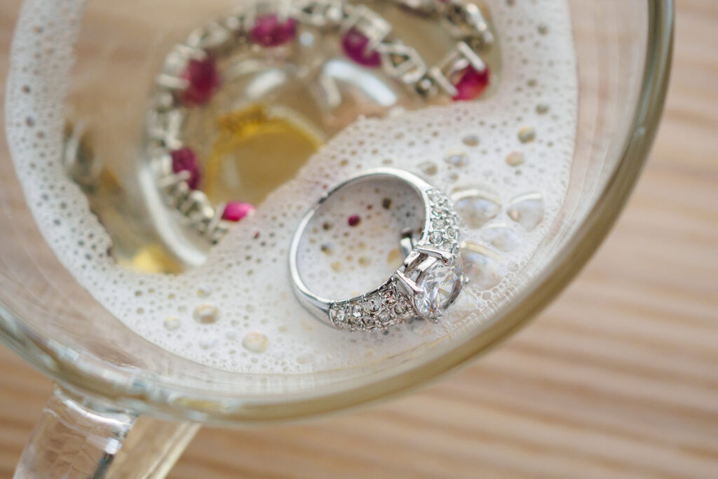 cleaning vintage jewelry diamond ring and bracelet in glass on wood table background