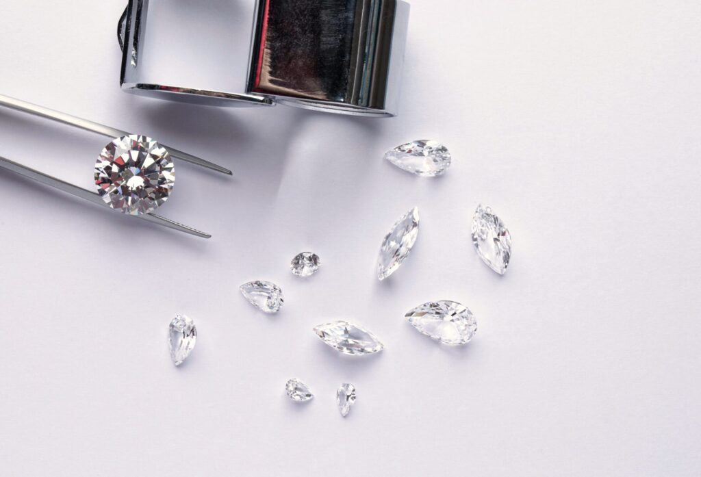 Polished diamonds of various sizes and shapes wit jewelry tools lie at the workplace of an expert examining the quality of stones on light background with copy space.